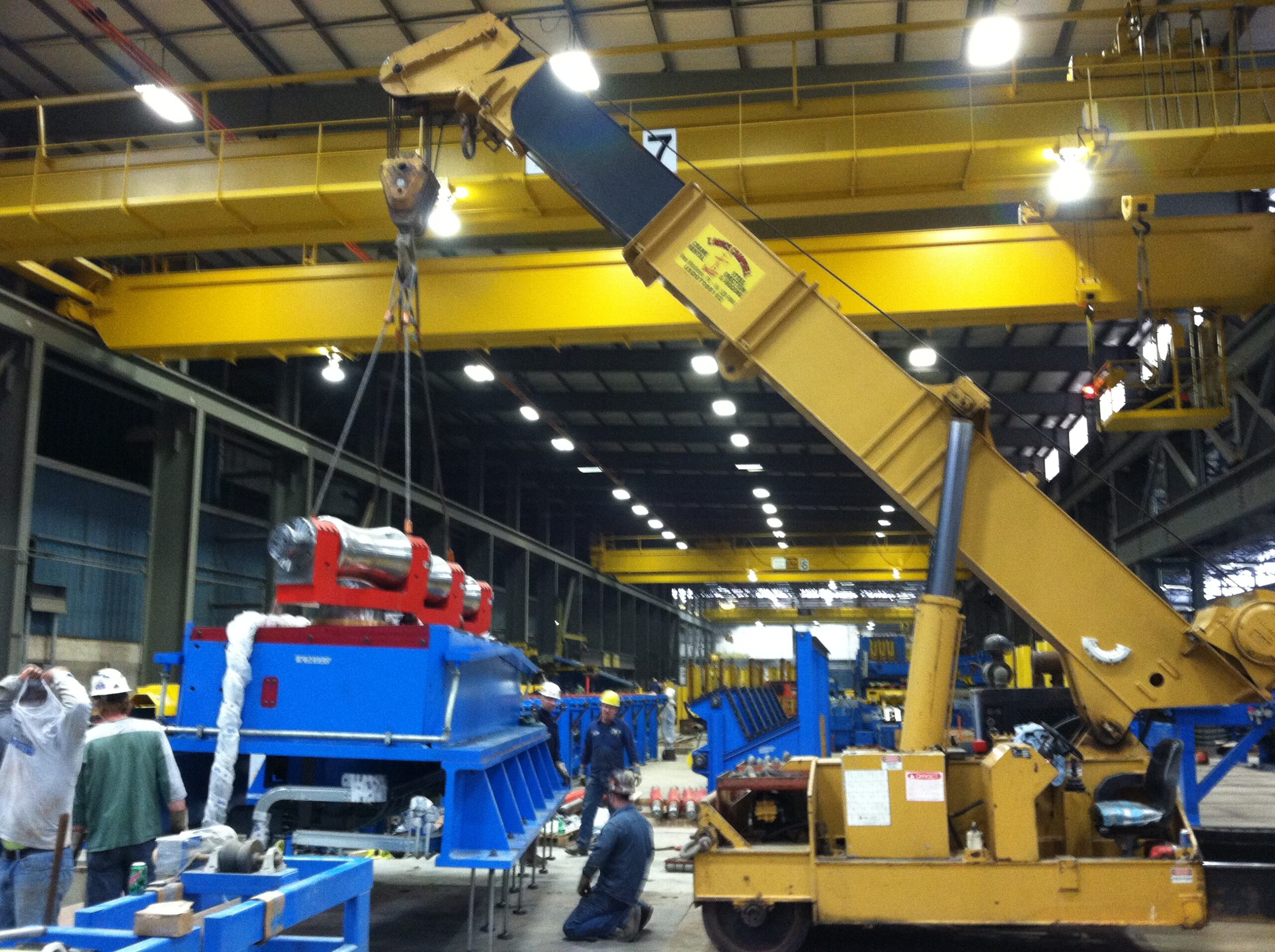 A construction crane elevating a blue machine above the ground.
